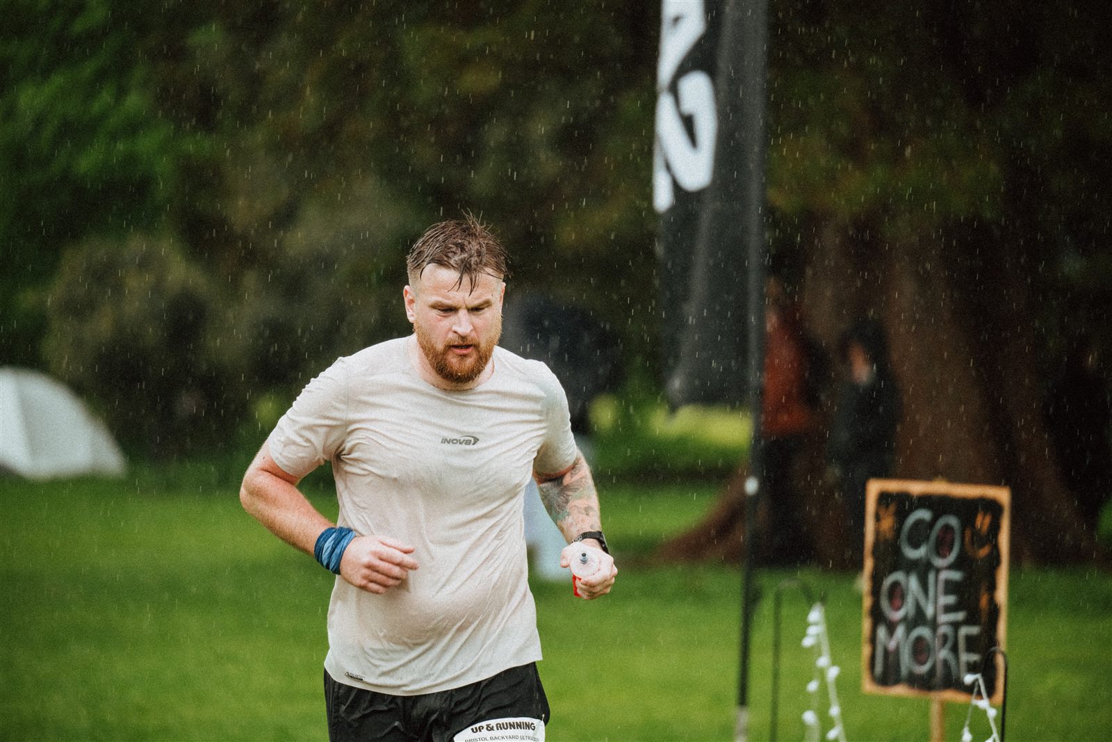 A Bristol Backyard Ultra runner moving through heavy rain near a sign reading go one more.